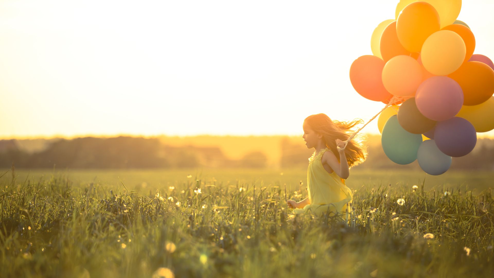 Girl holding balloons running on a meadow